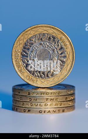 Studio shot of Sterling two pound coins in pile spelling out 'standing on the shoulders of giants' with an upright two pound coin balanced on top, aga Stock Photo