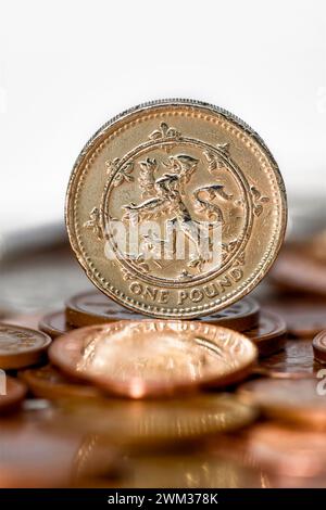 Studio shot of a one pound coin  in Sterling currency standing upright on table with out of focus coins in foreground against a white background Stock Photo