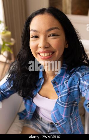 Young biracial woman smiles brightly at the camera on a video call Stock Photo