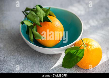 Blue ceramic bowl full of ripe oranges on concrete table Stock Photo