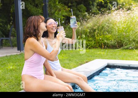 Biracial female friends enjoy a sunny day by the pool, with copy space Stock Photo