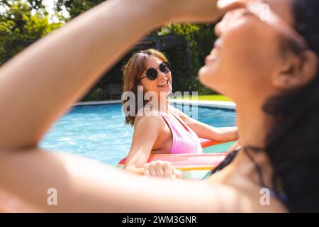 Biracial female friends enjoy a sunny day in the pool Stock Photo
