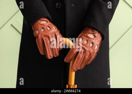 Man in stylish brown leather gloves with umbrella on green background, closeup Stock Photo