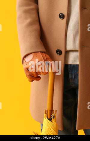 Man in stylish brown leather gloves with umbrella on yellow background, closeup Stock Photo
