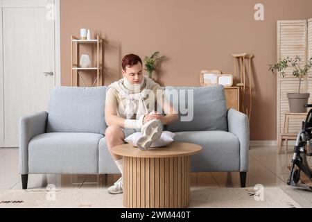 Injured young man after accident with his leg on pillow at home Stock Photo