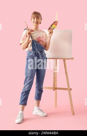Female artist with paint palette and easel on pink background Stock Photo