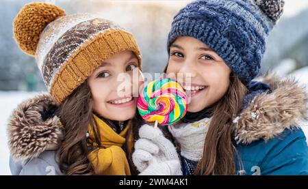 Two girls 12 15 years happy about a big lollipop bobble hat winter jacket portrait laughing beautiful eyes beautiful teeth winter ice snow cold cold Stock Photo