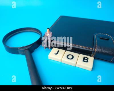 Notebook,miniature people and magnifying glass with text JOB on blue background. Stock Photo