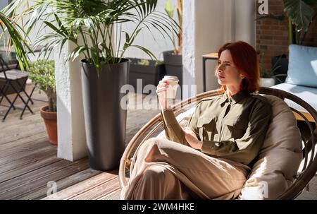 Young relaxed business woman taking work break drinking coffee sitting in chair. Stock Photo