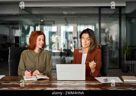 Two busy business women working together using laptop at desk in office. Stock Photo