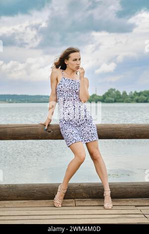 Pensive young woman touching her lip and looking away while standing on pier Stock Photo
