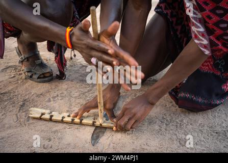 Two Maasai warriors use friction by rubbing sticks together to start a fire in a village in Mikumi, Tanzania. Stock Photo