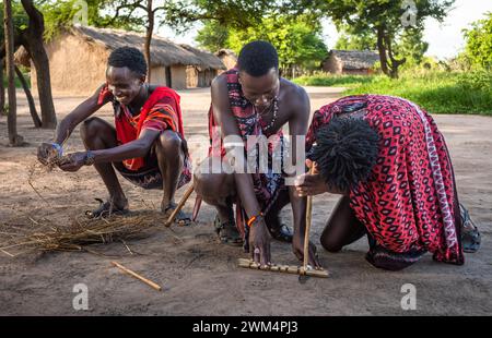 Two Maasai warriors use friction by rubbing sticks together to start a fire in a village in Mikumi, Tanzania. Stock Photo