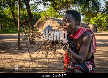 A Maasai warrior blows to start fire by friction after rubbing sticks together  in a village in Mikumi, Tanzania. Stock Photo