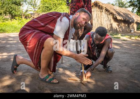 A Maasai warrior starts fire by friction after rubbing sticks together  in a village in Mikumi, Tanzania. Stock Photo