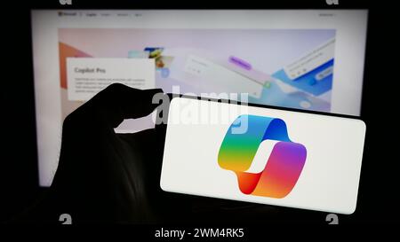 Person holding mobile phone with logo of artificial intelligence chatbot Microsoft Copilot in front of business web page. Focus on phone display. Stock Photo