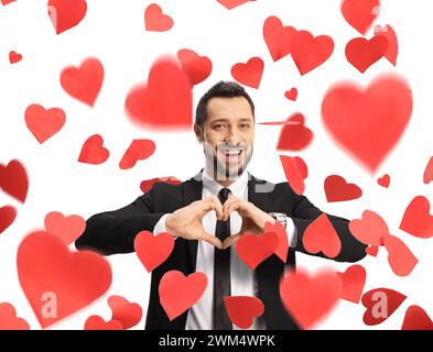 Young man in a suit and tie gesturing a heart symbol and standing under falling hearts isolated on white background Stock Photo