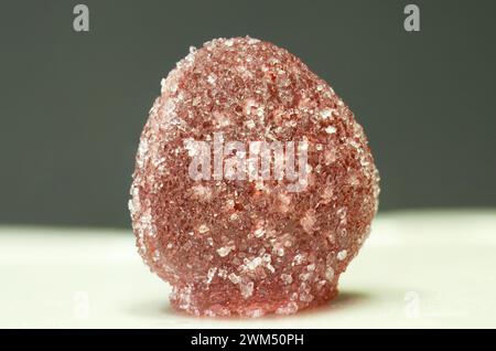 Sugar crystals sprinkled on red gumdrop jelly soft candy in selective focus isolated on dark green background Stock Photo