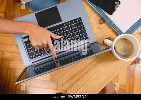 top view of unrecognizable brunette woman at home sitting touching laptop screen with finger on table, working with cup of coffee and notepad Stock Photo