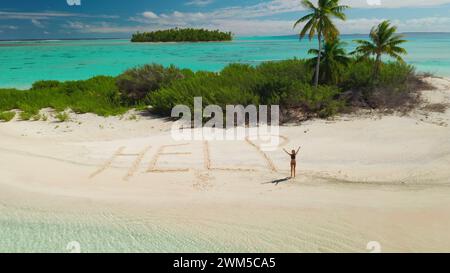 Aerial view lonely tropical inhabited island surrounded turquoise coral reef. Woman need rescue. Word HELP written on sand beach. Young female in bikini waving hands ask to save her. Drone flight Stock Photo
