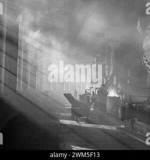 Train worker and locomotives in a beautiful sun light from a window- Chicago, Illinois. In the roundhouse at a Chicago and Northwestern Railroad yard - Jack Delano photo 1942 Stock Photo