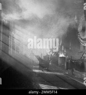 Train worker and locomotives in a mysterious sun light - Chicago, Illinois. In the roundhouse at a Chicago and Northwestern Railroad yard - Jack Delano photo 1942 Stock Photo