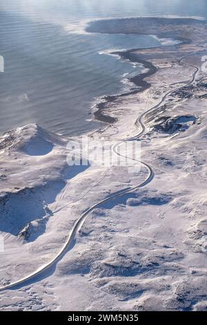 Aerial view of a winding road along the edge of a green lake surrounded ...