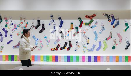 Zhuji, China's Zhejiang Province. 24th Feb, 2024. A woman walks past an exhibition wall of a sock company in Zhuji, east China's Zhejiang Province, Feb. 24, 2024. Production lines of sock companies in east China's Zhuji City, dubbed as 'the sock capital,' are operating at full swing to meet the orders. As the world's largest sock manufacturing base, the Datang sub-district of Zhuji in Zhejiang Province produces approximately 25 billion pairs of socks yearly, accounting for more than 70 percent of the output of China and one-third of the whole world. Credit: Xu Yu/Xinhua/Alamy Live News Stock Photo