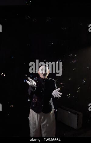 Minimal portrait of mime artist playing with soap bubbles on stage against black background Stock Photo