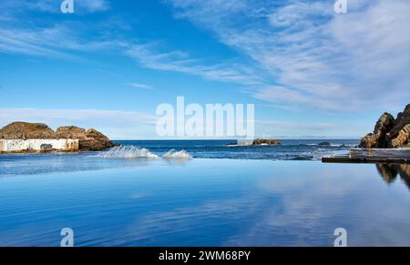 Tarlair Open Air Swimming Pools Macduff Scotland a blue sky and the sea at high tide rushing in to fill the pool Stock Photo
