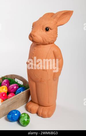 Eine Osterhasenfigur aus Ton vor einem Korb mit Ostereiern *** A clay Easter bunny figure in front of a basket of Easter eggs Stock Photo