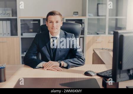 Serene executive poses at his desk with a confident, pensive look in a modern office. Stock Photo