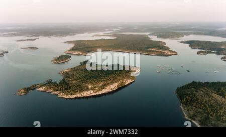 The soft light of dusk settles over a sprawling archipelago, where fish farms dot the tranquil waters between forested islands. The vastness of the scene emphasizes the harmony of industry and nature. Stock Photo