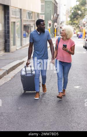 Interracial couple walking on a sidewalk holding hands. Young man and ...