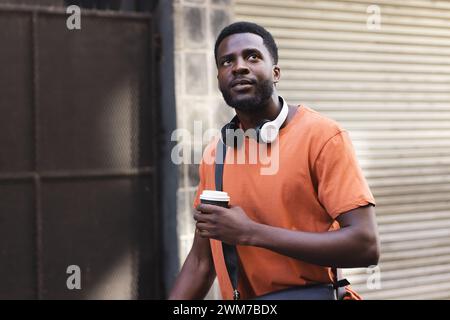A young African American man holds a coffee cup outdoors in the city Stock Photo