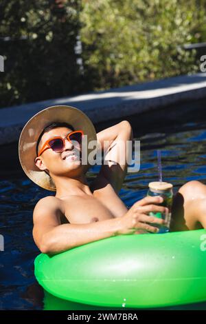 Young Asian man enjoys a sunny day floating in a pool, with copy space Stock Photo