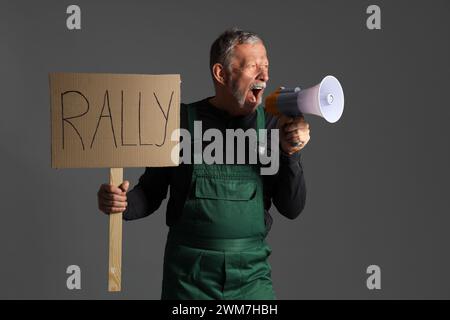 Protesting miner man with placard shouting into megaphone on dark background Stock Photo