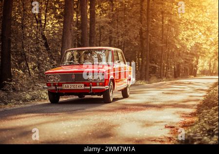 classic VAZ 2103 sedan from 1970s on forest road. Red Lada shot during golden hour - three quarter front view. Stock Photo