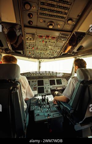 inside pilot's cabin of Airbus A320-212 (registration UR-WRM). Warm toned vertical image of two pilots sitting in cockpit of passenger aircraft. Stock Photo