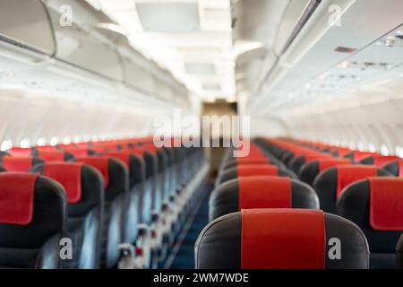 Economy class with red headrest covers. Perspective view of empty passenger airplane interior with focus on seats closer to camera. Stock Photo