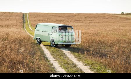 Green classic Volkswagen Transporter van on countryside unpaved downhill road, three quarter view. Stock Photo