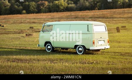 Green classic Volkswagen Transporter bus on countryside dirt road, rear three quarter view Stock Photo