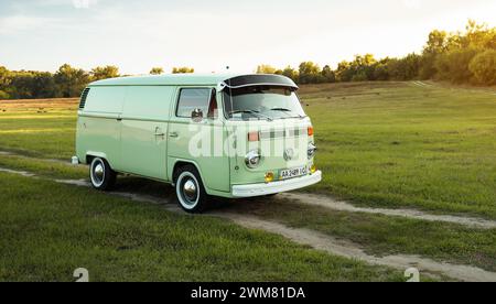 Green classic Volkswagen Transporter bus on countryside unpaved road, front three quarter view. Stock Photo