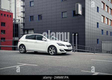 white Peugeot 308 hatchback in front of the corner of anthracite modern building. three quarter view of compact car Stock Photo