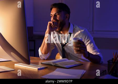 Tired man with coffee working late in office Stock Photo