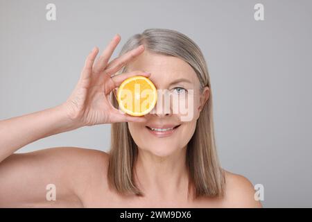 Beautiful woman with half of orange rich in vitamin C on grey background Stock Photo