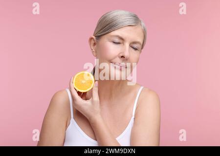 Beautiful woman with half of orange rich in vitamin C on pink background Stock Photo