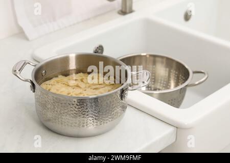Cooked pasta in metal pot on countertop near sink Stock Photo