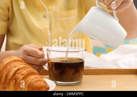 Woman pouring milk into cup with hot drink in bed, closeup Stock Photo