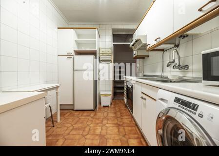 Kitchen furnished with antique white furniture with wooden handles, column unit with integrated refrigerator, microwave oven on the white countertop a Stock Photo